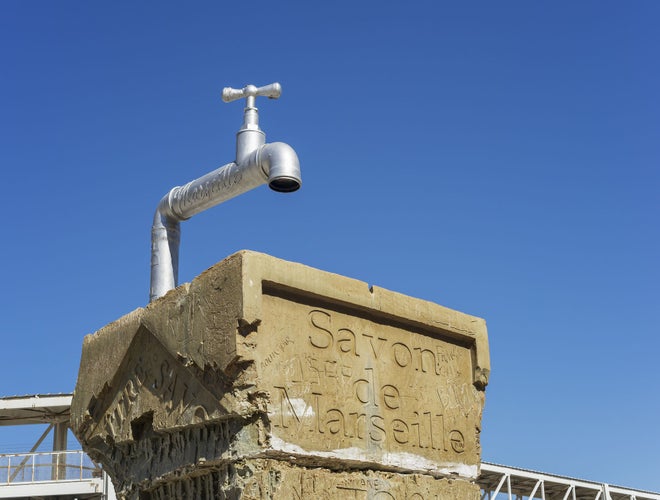 Art installation of a giant faucet on a carved block featuring -Savon de Marseille,- a tribute to the city’s famous traditional soap, under a clear blue sky.jpg