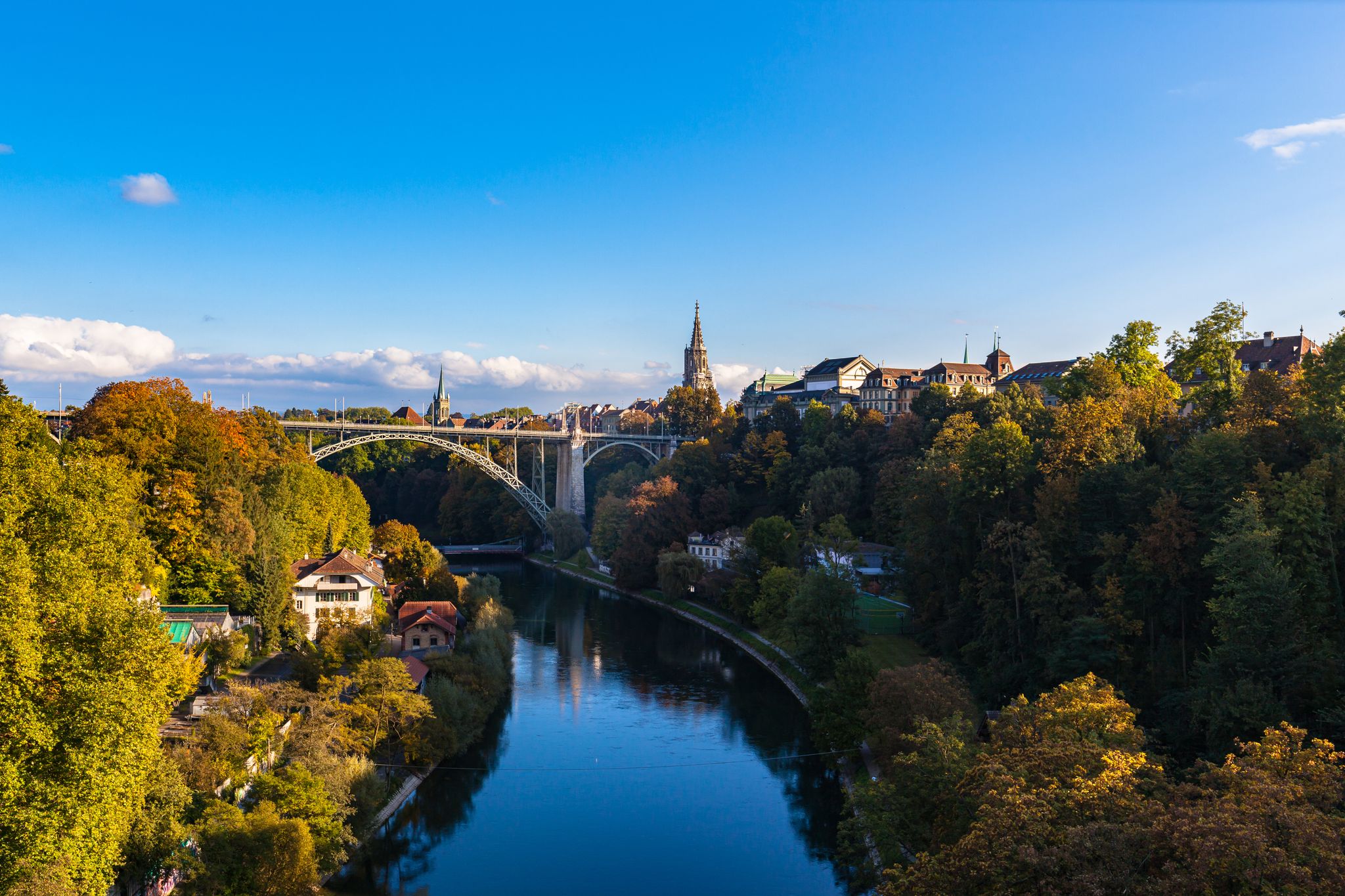 photo of beautiful view of Aare River and Bern old town with Bern Minster (Münster) cathedral and Kornhausbrücke (Kornhaus bridge) from Lorrainebrücke on sunny autumn day with blue sky, Switzerland.