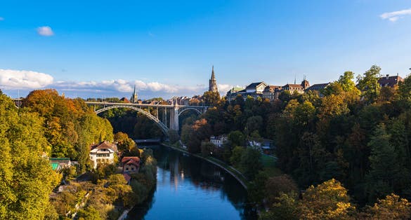 photo of beautiful view of Aare River and Bern old town with Bern Minster (Münster) cathedral and Kornhausbrücke (Kornhaus bridge) from Lorrainebrücke on sunny autumn day with blue sky, Switzerland.