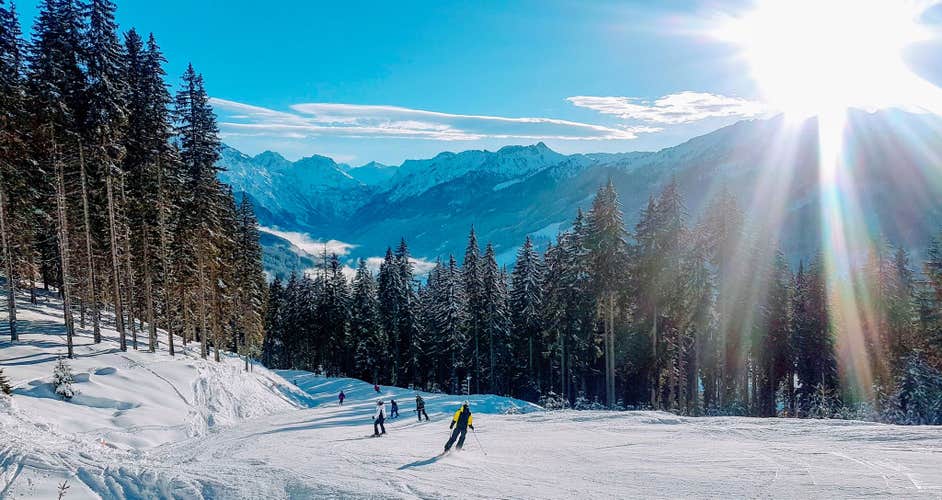 photo of people skiing around ski resort of Flachauwinkl. LENS FLARE Winter sunbeams shine on skiers riding down the slopes in Austrian Alps. Tourists having fun skiing in the breathtaking mountains in Austria.