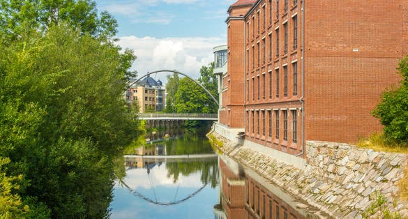 Photo of View on the calm river with reflection in Chemnitz, Germany. Former industrial building on the one bank and a small bridge over the river. Concept of new and old.