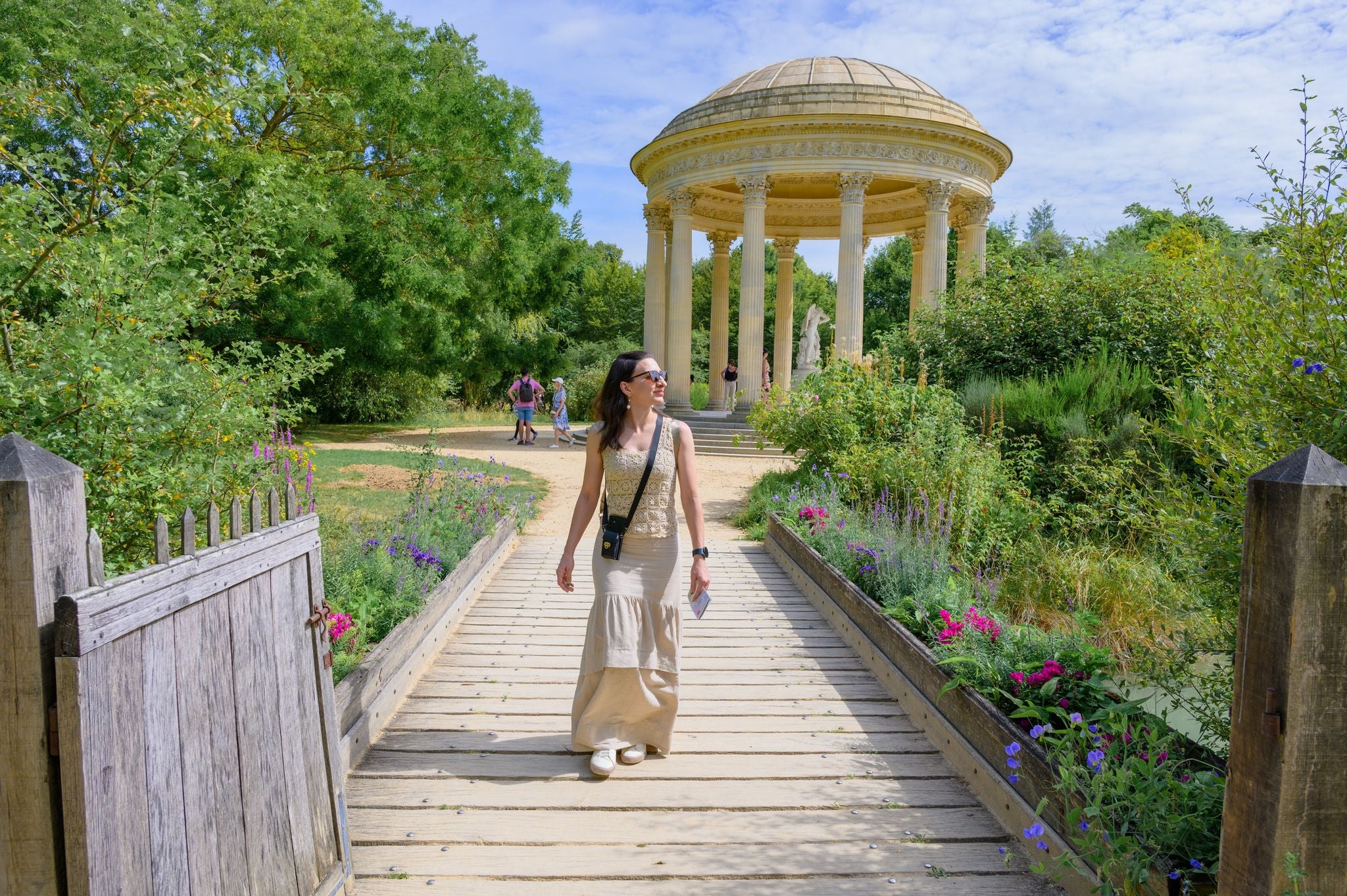 Solo female tourist in pastel (light) colored clothing walking around the grounds of the Palace of Versailles in Paris, France.