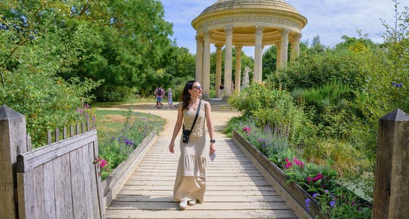Solo female tourist in pastel (light) colored clothing walking around the grounds of the Palace of Versailles in Paris, France.