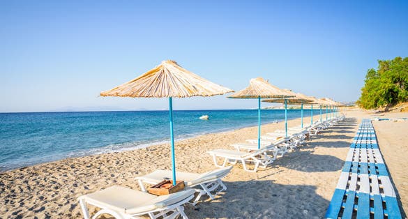 Beach, Greece, Kos Island, Kardamena: beautiful holiday setting on a secluded beach with umbrellas on the Greek Aegean Sea with turquoise waters and a picturesque bay and islands in the background