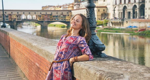 photo of relaxed young woman on embankment near ponte vecchio in florence, italy.