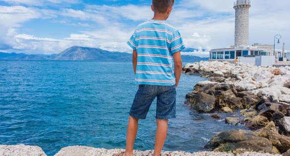 Back view of cute boy looking at the Patras lighthouse, Peloponnese, Greece. The lighthouse located on the seafront near Saint Andrew's Cathedral, is the symbol of Patras Town.