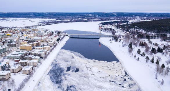 Photo of beautiful winter landscape with buildings and a bridge over Ounasjoki River in Rovaniemi, Finland.