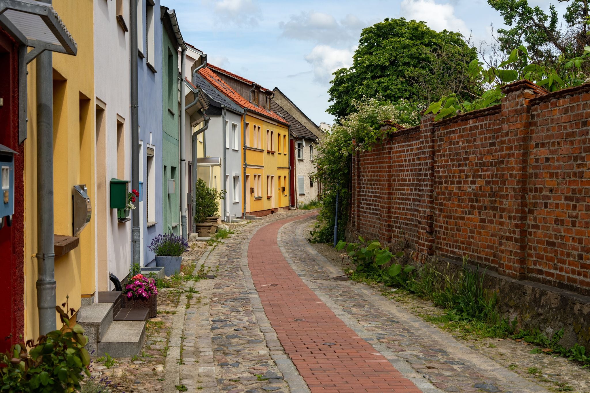 photo of view of historic cobblestone street with colorfully painted houses and a brick wall in the old tow of Barth (Mecklenburg-Vorpommern, Germany) during summer.
