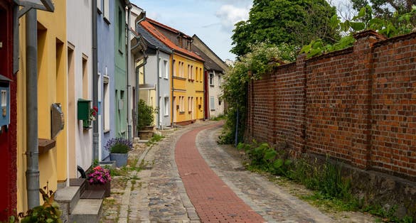 photo of view of historic cobblestone street with colorfully painted houses and a brick wall in the old tow of Barth (Mecklenburg-Vorpommern, Germany) during summer.