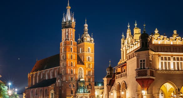 Krakow, Poland. Evening Night View Of The St. Mary's Basilica And Cloth Hall Building. Famous Old Landmark Church Of Our Lady Assumed Into Heaven. Saint Mary's Church. UNESCO World Heritage Site.