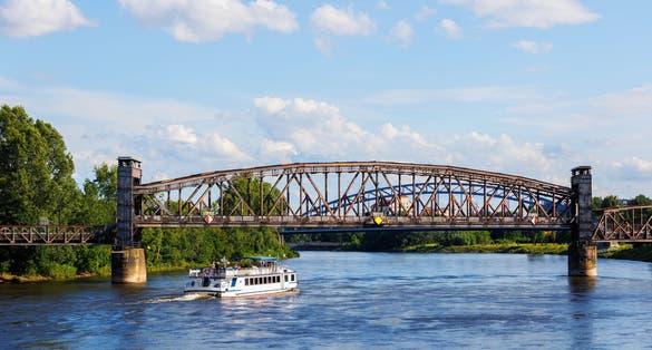 Tourist boat cruises under old historic iron bridge on Elbe River in Magdeburg, Germany with blue sky clouds background landscape. Saxony-Anhalt center cityscape sightseeing water trip