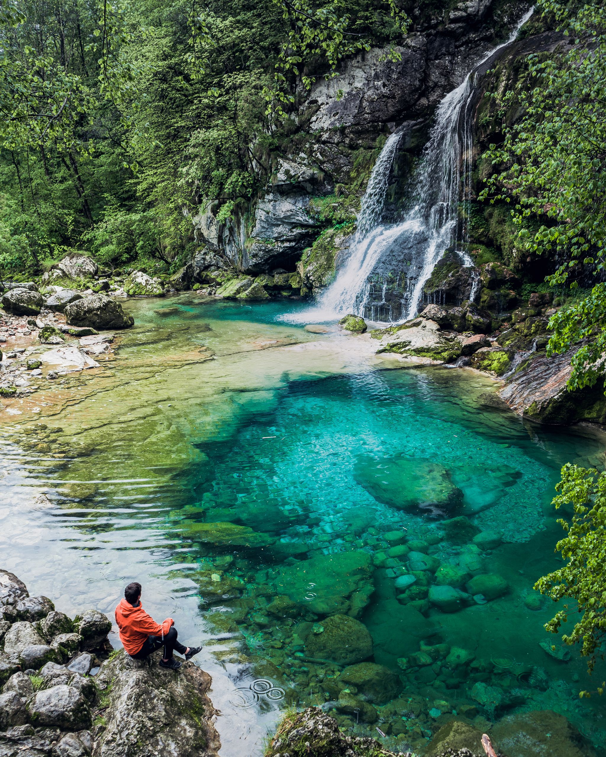 Traveler Man enjoying serene view of Crystal clear water and small pond with waterfalls in the middle of the forest. Drinking water. Slap Virje, Virje waterfall, Bovec, Slovenia, Julian Alps.