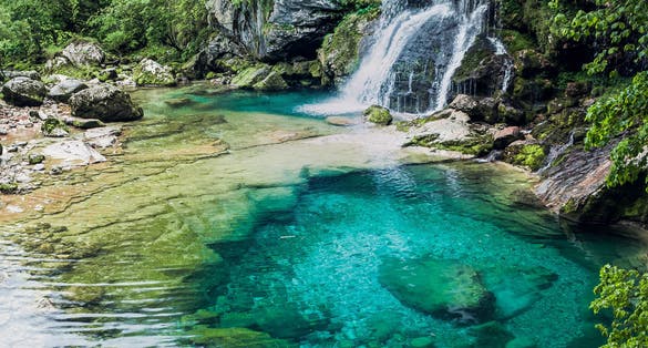 Traveler Man enjoying serene view of Crystal clear water and small pond with waterfalls in the middle of the forest. Drinking water. Slap Virje, Virje waterfall, Bovec, Slovenia, Julian Alps.