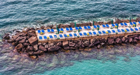 Photo of beach chairs and umbrella on a breakwater in Sorrento, Italy.