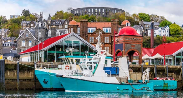 photo of view of A view of boats moored by the landing stage in the town of Oban, Scotland from Oban Bay on a summers day.