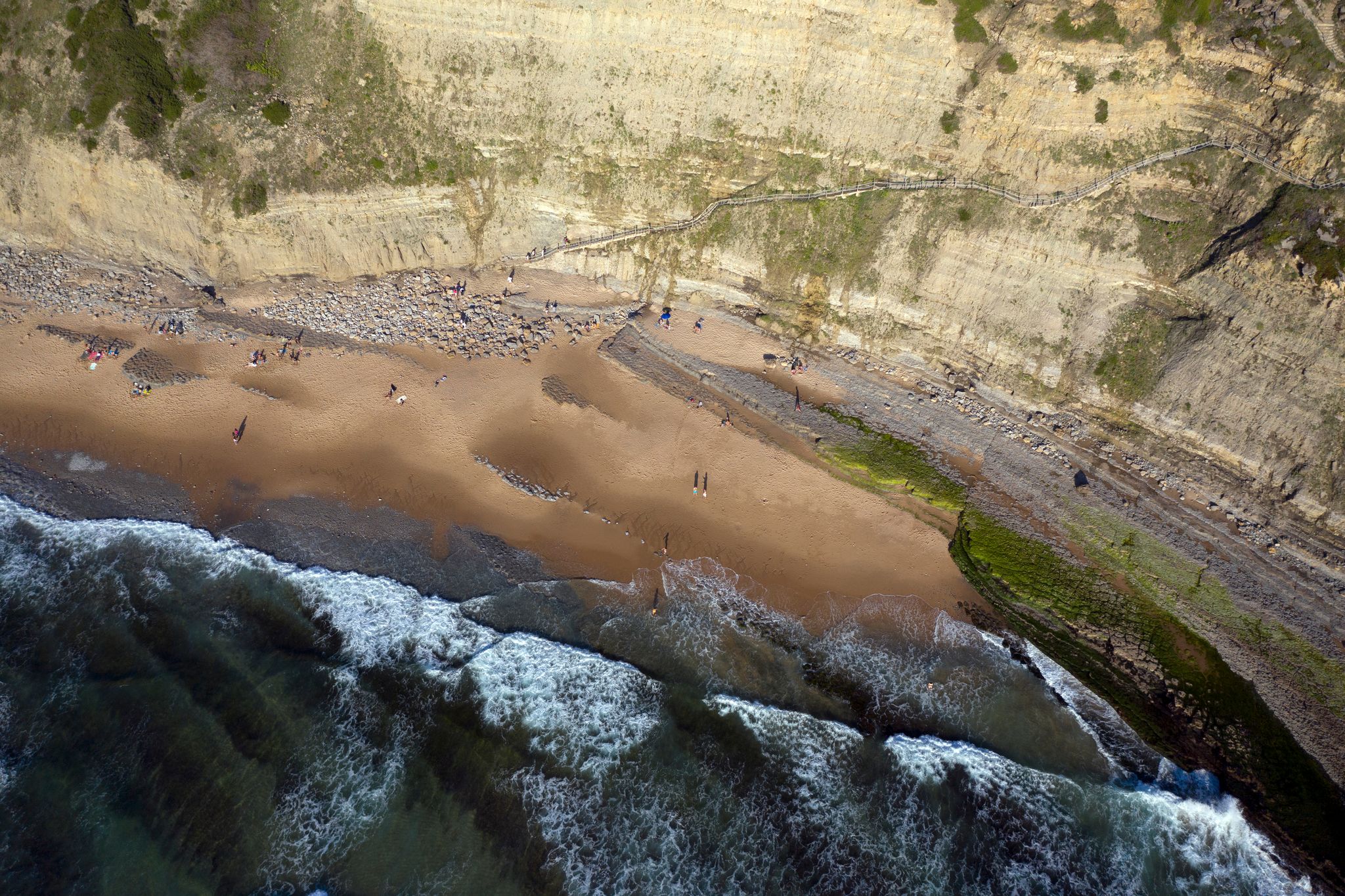 Aerial birds eye view of "Praia da Aguda" beach in Sintra, Lisbon - Portugal. Breaking waves and huge cliffs.