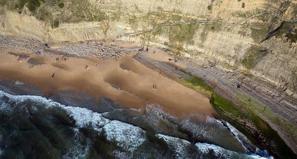 Aerial birds eye view of "Praia da Aguda" beach in Sintra, Lisbon - Portugal. Breaking waves and huge cliffs.