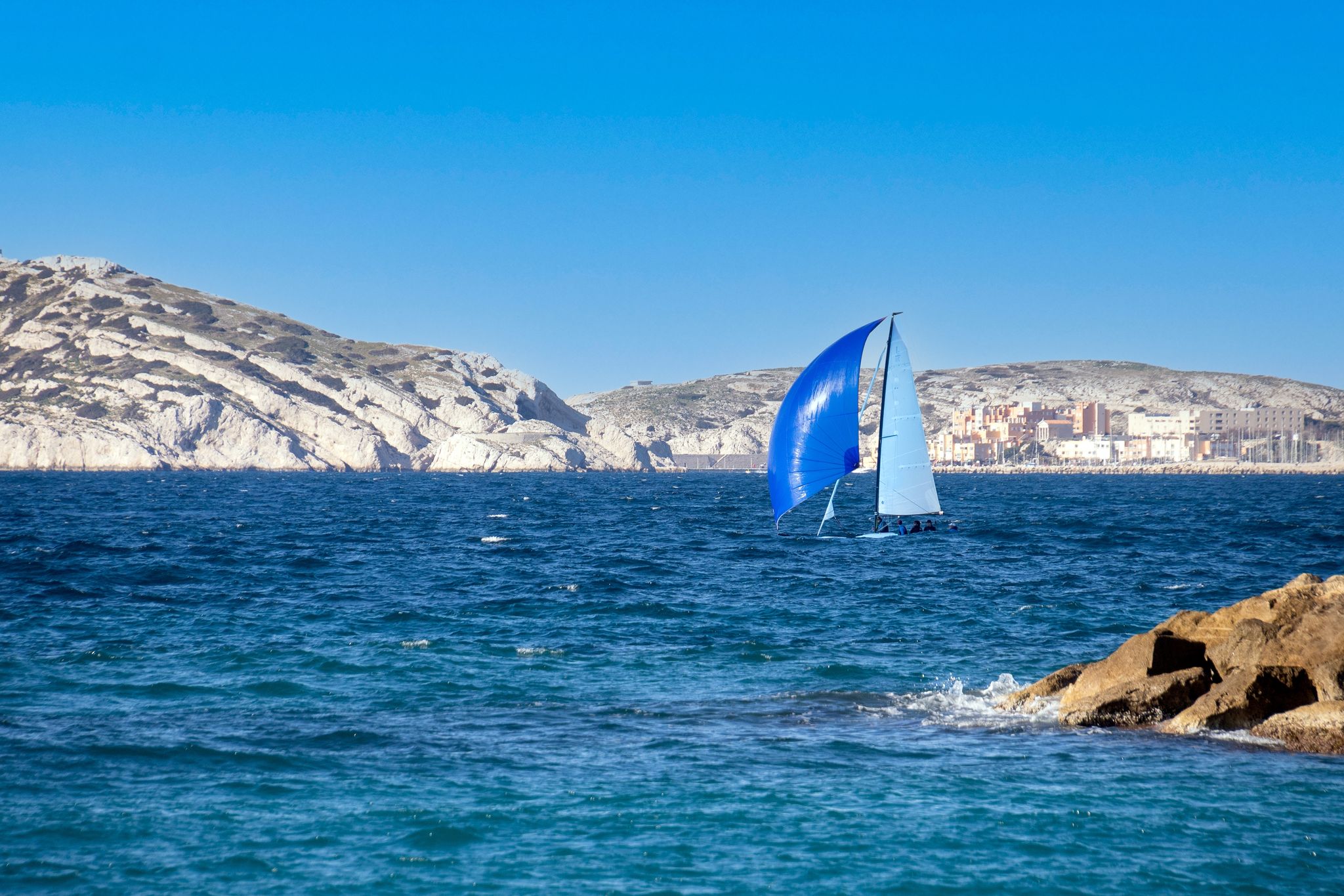 Blue sailboat seen from Prado Beach in Marseille, with sea and rocky coastline in the background..jpg