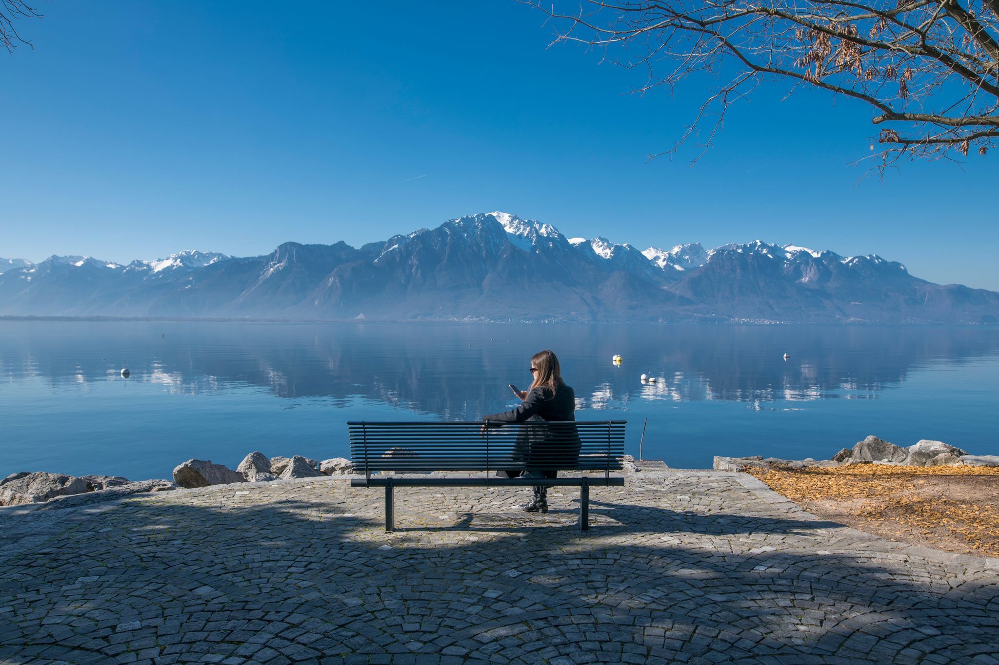 Bench on the Montreux Riviera promenade with a view to mountains Alps Evian and Leman Geneva lake. Girl sitting and enjoying the landscape.