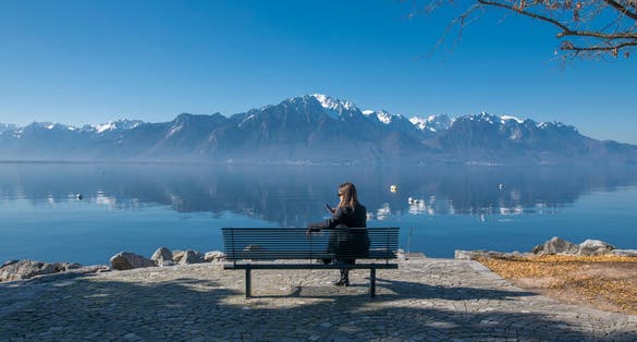 Bench on the Montreux Riviera promenade with a view to mountains Alps Evian and Leman Geneva lake. Girl sitting and enjoying the landscape.