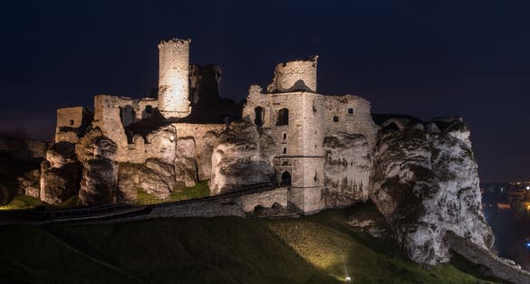 Photo of ruins of Ogrodzieniec Castle illuminated in the night in the south-central region of Poland.