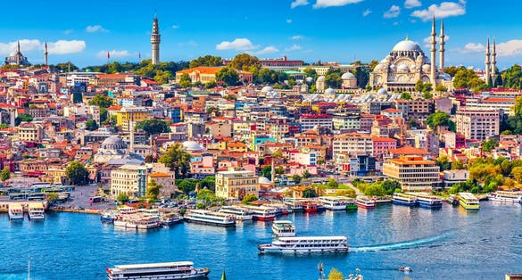 Touristic sightseeing ships in Golden Horn bay of Istanbul and mosque with Sultanahmet district against blue sky and clouds. Istanbul, Turkey during sunny summer day.