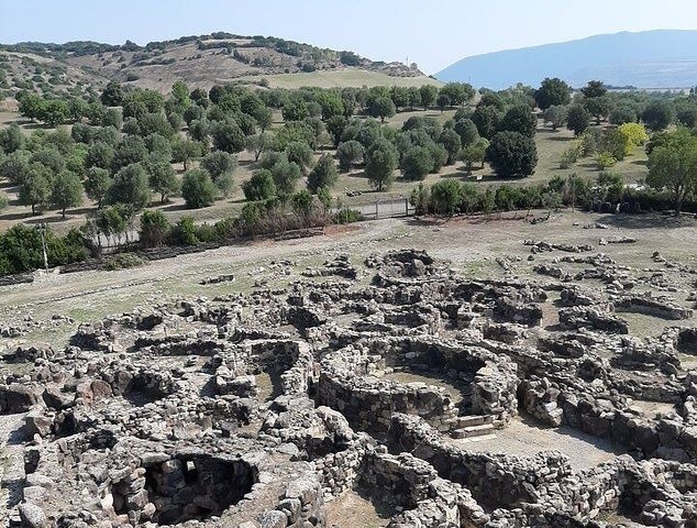 The Su Nuraxi surrounded by green trees and rolling hills under a clear blue sky..jpg