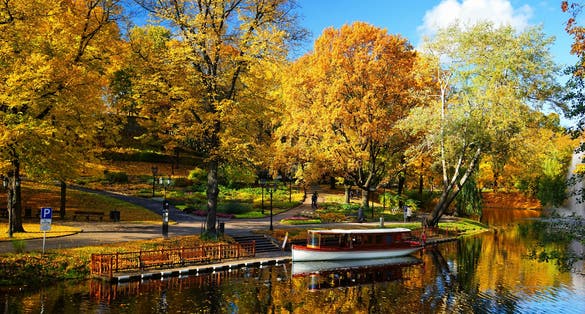 City park of the city of Riga with a canal with bright autumn leaves against the blue sky and reflections in the water