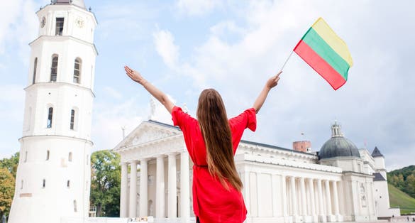 photo of young female tourist standing with lithuanian flag on the cathedral square in front of the famous basilica in vilnius. Having great vacations in Lithuania.