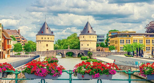photo of view of Kortrijk cityscape with Lys river, Broel Towers Gothic style buildings and Bridge in historical centre, red flowers on bridge fence, Fortification towers, belgium landmark, Flemish Region, Belgium