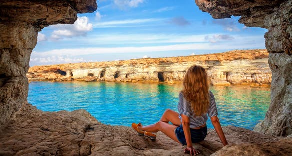 View from sea cave near Cape Greko(Capo Greco) of Ayia Napa and Protaras on Cyprus, Mediterranean Sea. Attractive woman enjoys the sea air on seaside. Holidays at Ayia Napa Resort, Cyprus