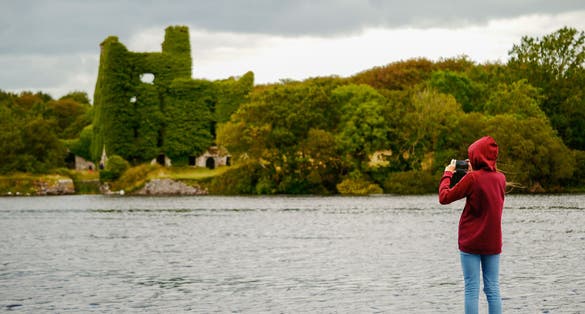 photo of Girl teenager taking picture on her smart phone of Menlo castle, Ireland, Galway, Concept: tourist, adventure, technology,