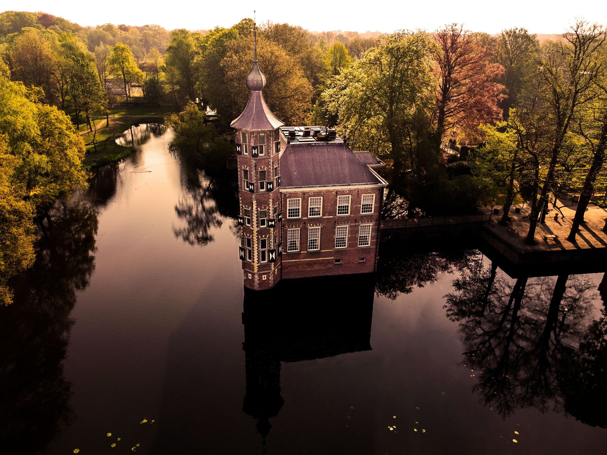 photo of an aerial view of a beautiful Breda Castle in a forest surrounded by water in Breda, the Netherlands.