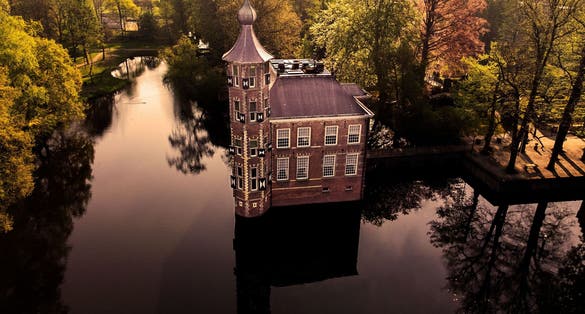 photo of an aerial view of a beautiful Breda Castle in a forest surrounded by water in Breda, the Netherlands.