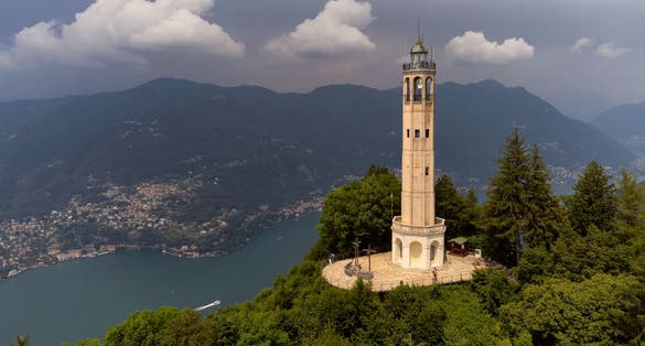 Aerial view of the Faro Voltiano (Volta Lighthouse) in Brunate, with the skyline of Lake Como, green forest and trees near Milan, Italy