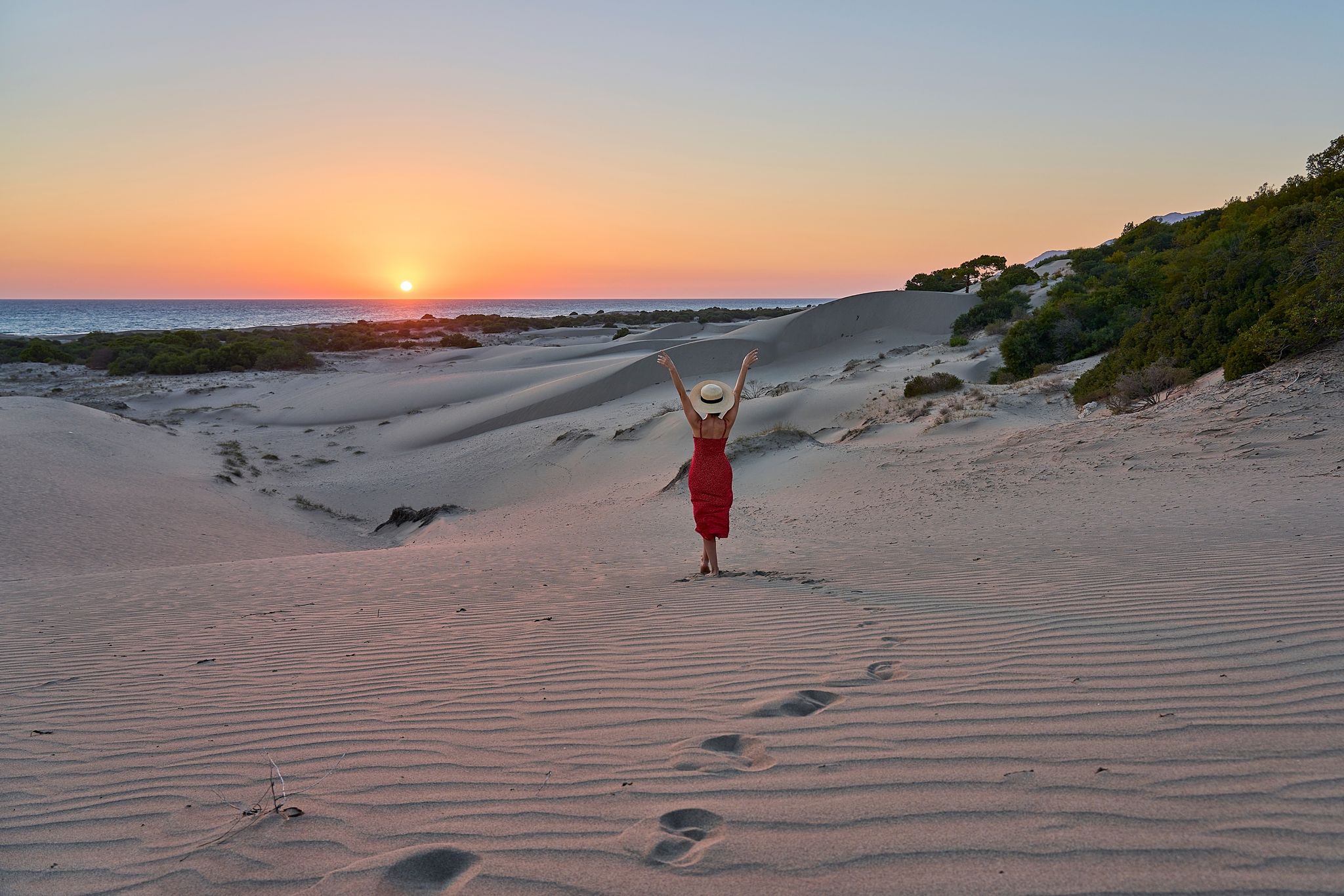photo of girl with hat and red dress is posing and watching amazing sunset landscape at sand dunes of Patara beach, Antalya, Turkey.