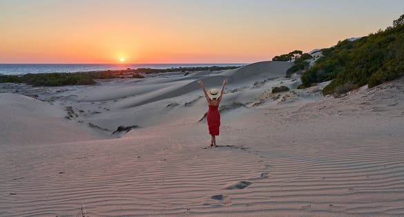photo of girl with hat and red dress is posing and watching amazing sunset landscape at sand dunes of Patara beach, Antalya, Turkey.