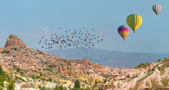 photo of hot air balloon flying over spectacular Uchisar castle and Pigeon valley in Cappadocia, Turkey.