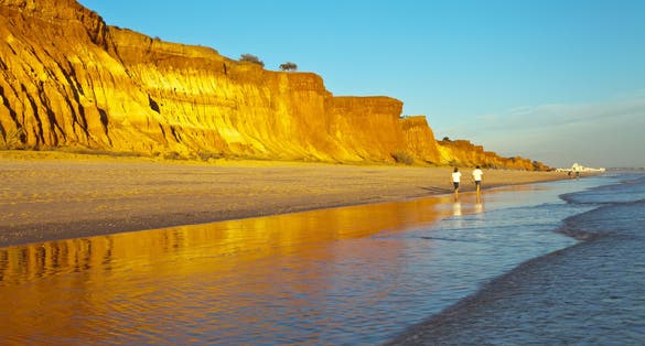 Portugal. Beautiful seascape of sandy Praia da Falesia beach in Algarve with unusual terracotta sculptural rocks attracts tourists for a seaside vacation. Summer family holidays. People out of focus