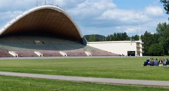 photo of Vilnius ,Lithuania - May 20, 2016: Tourists have rest on a spring lawn near the largest in Europe song theater scene in vingis park. The record of the viewers at a concert - 60 thousand in 1997.
