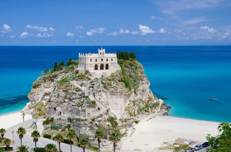 Monastery Sanctuary church of Santa Maria dell Isola on top of rock Tyrrhenian Sea and green palm trees, blue sky white clouds in summer clear day, Tropea town.