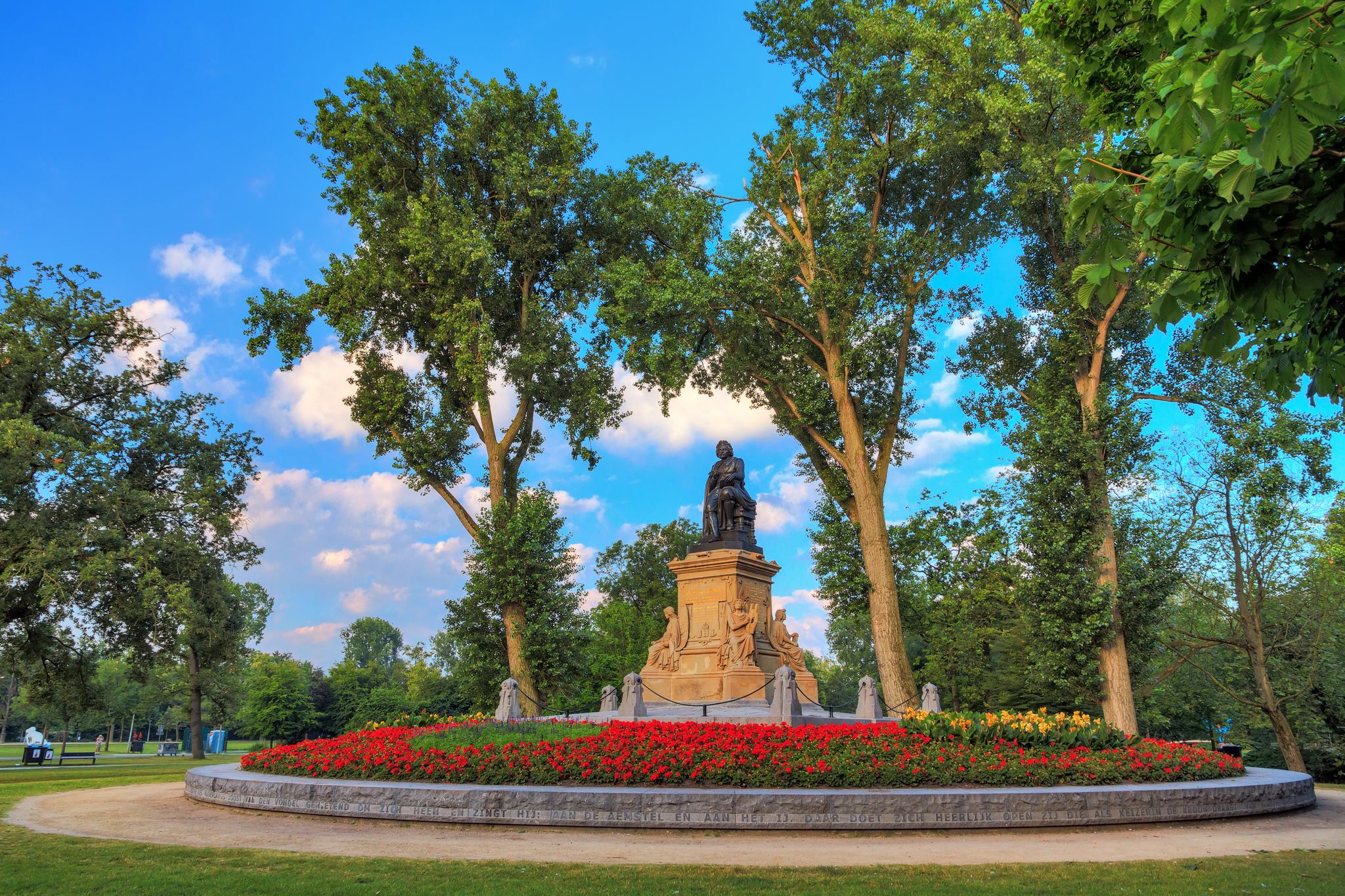 Photo of statue of Joost van den Vondel (1867) with tulips in the Vondelpark in Amsterdam, the Netherlands, on a beautiful spring morning.