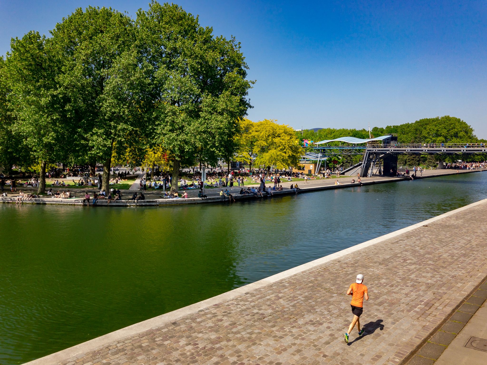 photo of a man running at La Villette while people are having picnic in Paris, France.