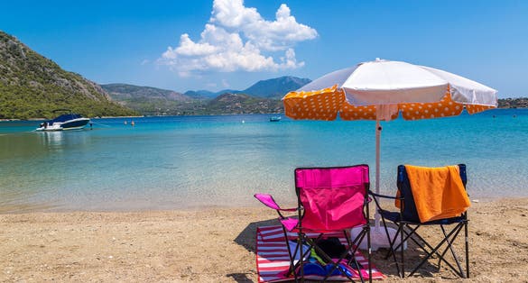 Photo of umbrella and sundecks on beautiful sandy beach near Loutraki in a summer day with blue sky, Greece.