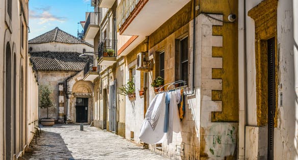 A small residential alley with laundry hanging from a window leads to the entrance of the Church of San Giovanni al Sepolcro in the city of Brindisi, Italy