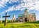 Photo of colorful morning shot of the famous Bagrati Cathedral in Kutaisi, Georgia, with beautiful clouds over blue sky, green grass and a large Christian cross in front of the building.