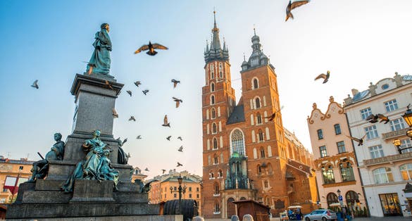 Photo of old city center view with Adam Mickiewicz monument, St. Mary's Basilica and birds flying in Krakow ,Poland.