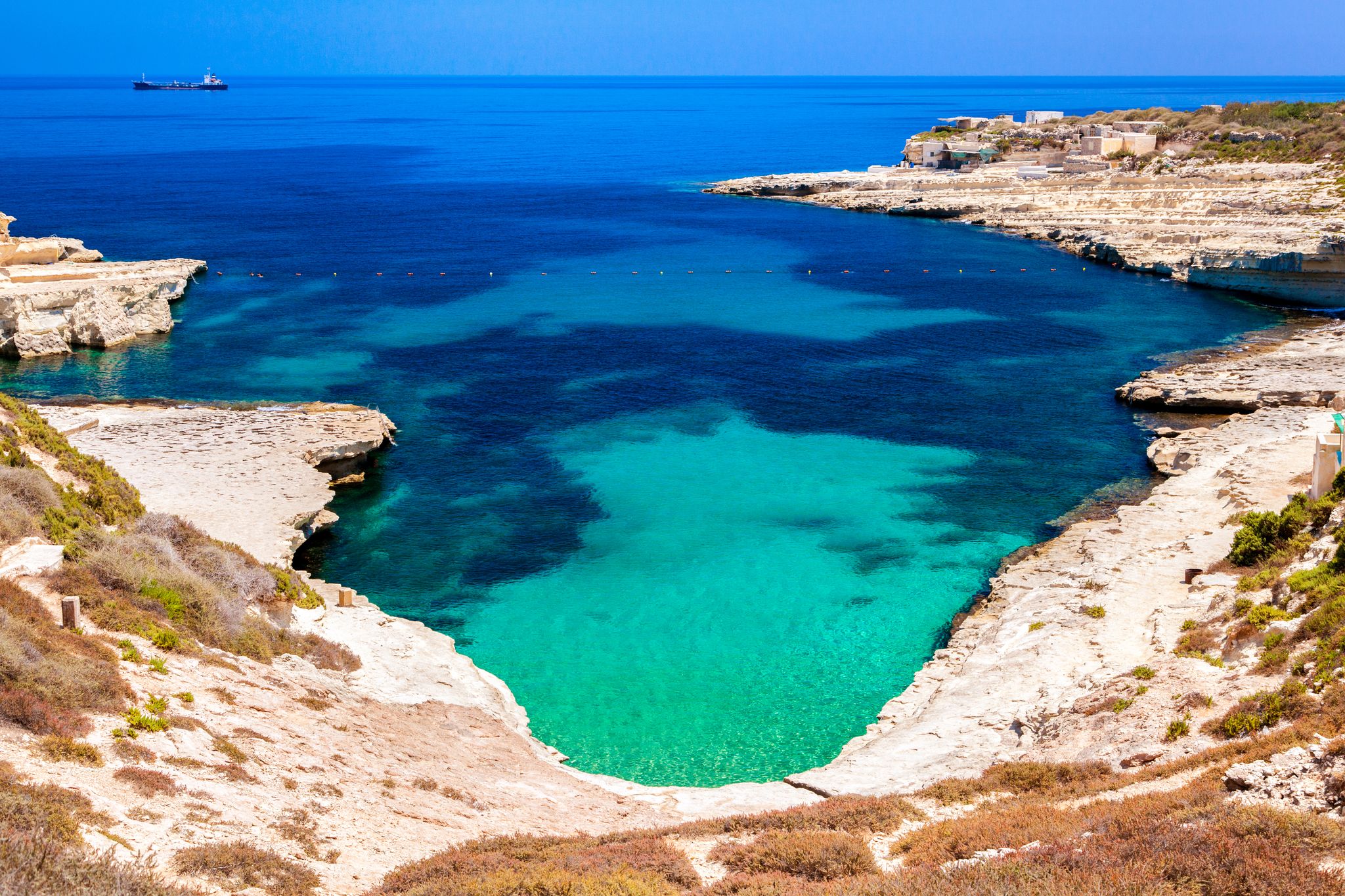 Photo of crystal clear turquoise water in blue lagoon of St. Peters pool  rocky beach at Malta.