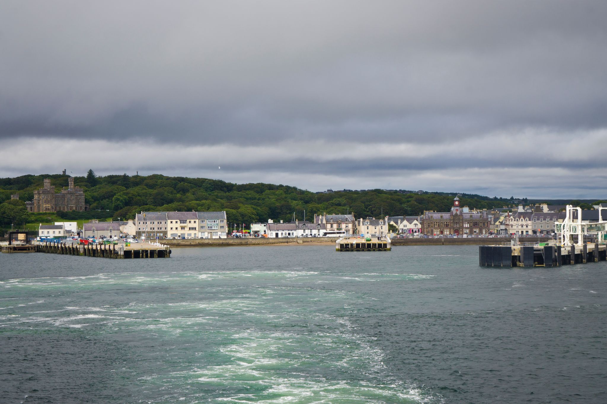 photo of The view of the port in Stornoway: city streets, commercial harbor with docks and the ferry terminal. The Lewis Castle surrounded by vast green grounds is visible in the background. Scotland.