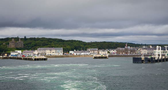 photo of The view of the port in Stornoway: city streets, commercial harbor with docks and the ferry terminal. The Lewis Castle surrounded by vast green grounds is visible in the background. Scotland.